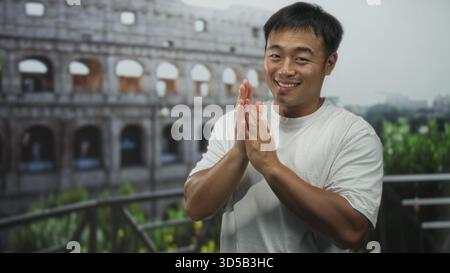 Homme en t-shirt blanc se tient sur la terrasse avec les mains pressées ensemble à côté du bâtiment du colisée romain ; gratitude. Banque D'Images