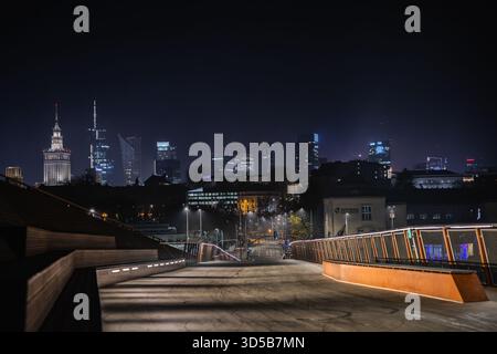 Une vue nocturne de Varsovie capturée depuis une passerelle moderne, avec des gratte-ciels brillants et le Palais de la culture qui brille au loin. Banque D'Images