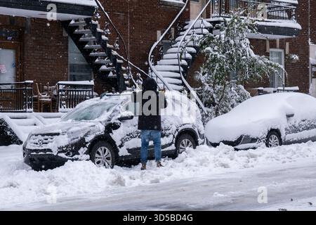 Montréal, CA - 11 novembre 2025 : sur la rue Laurier, un homme dégage activement la neige épaisse d'une voiture stationnée à l'aide d'un balai à neige Banque D'Images