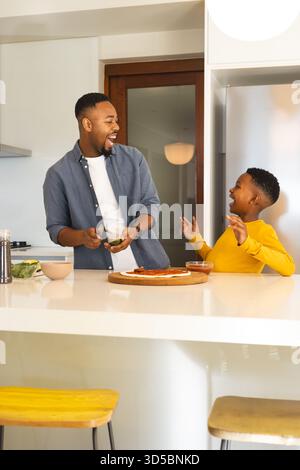 Père et fils riant tout en préparant une pizza ensemble dans une cuisine moderne Banque D'Images