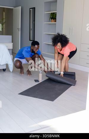 Couple afro-américain roulant tapis de yoga à la maison, se préparant pour l'entraînement ensemble Banque D'Images