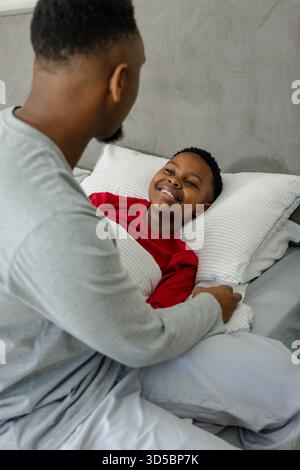 Père afro-américain réconfortant son fils au lit, partageant un moment chaleureux à la maison Banque D'Images