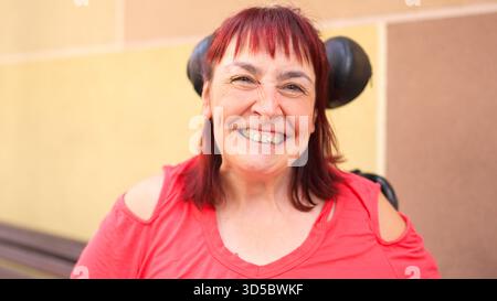 Femme avec les cheveux roux souriant et heureux en fauteuil roulant à l'extérieur Banque D'Images