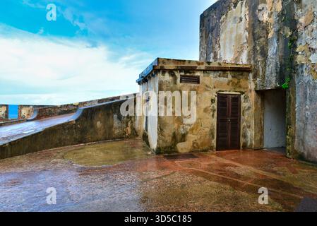 Une vieille structure en béton se dresse contre un mur de pierre altérée, le sol paraissant récemment humide par la pluie. Banque D'Images