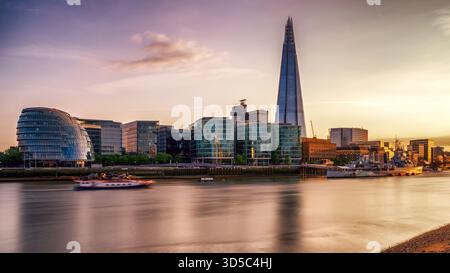 Les gratte-ciel londoniens au coucher du soleil avec le gratte-ciel Shard et les bâtiments modernes au bord de la rivière se reflètent dans la calme Tamise, montrant une architecture emblématique Banque D'Images