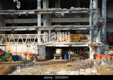 Excavatrices lourdes et machines travaillant sur les ruines d'un bâtiment urbain partiellement démoli avec une grande structure en béton courbée en arrière-plan. Banque D'Images
