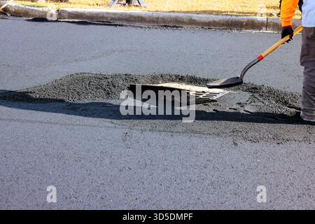 Travailleur utilise la pelle pour remplir le nid de poule avec de l'asphalte dans le quartier résidentiel pendant les travaux de route Banque D'Images