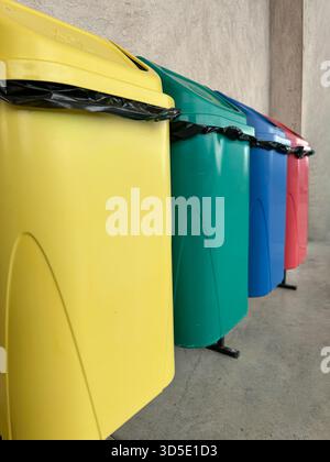 Rangée de bacs de recyclage colorés utilisés pour la séparation des déchets dans un espace public. L'image montre des conteneurs jaunes, verts, bleus et rouges alignés sur un Banque D'Images