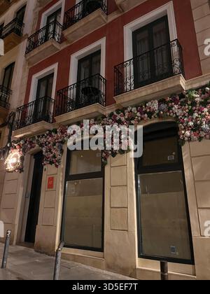 Une charmante façade dans la vieille ville d'Alicante avec un bâtiment rouge et crème avec des balcons en fer forgé et des décorations florales abondantes. Banque D'Images