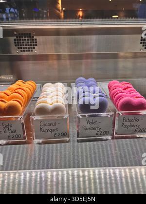 Un présentoir de boulangerie en verre rempli de macarons colorés étiquetés avec différentes saveurs. La vitrine vibrante des desserts est photographiée à Hull, en Angleterre. Banque D'Images
