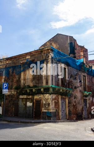 Vieux bâtiment en ruine avec des bâches bleues et graffiti sur Un coin de rue urbaine calme aujourd'hui Banque D'Images