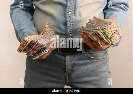 Les deux mains saisissent de lourds paquets de billets de banque monnaie ukrainienne. symbolisant l'accumulation financière, le montant important de trésorerie et l'activité économique. argent liquide Banque D'Images