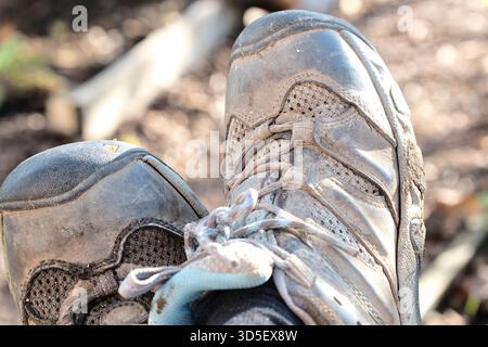 Pieds de jardinier reposant dans des bottes usées après avoir travaillé sur une parcelle d'allotissement, avec des plantes et des structures de jardin en arrière-plan, Royaume-Uni. Banque D'Images
