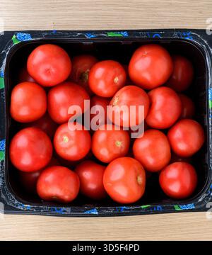 Vue de dessus de tomates rouges fraîches mûres disposées dans une caisse en plastique noir placée sur une table en bois rustique. Banque D'Images
