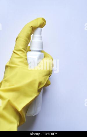 Main dans un gant jaune tenant le flacon pulvérisateur blanc sur fond blanc propre Banque D'Images