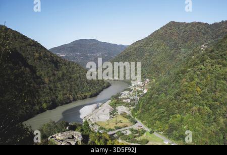 Vue aérienne d'une rivière serpentant à travers des montagnes verdoyantes en Adjara, Géorgie, avec de petits villages nichés le long de la vallée sous un ciel bleu clair, c Banque D'Images