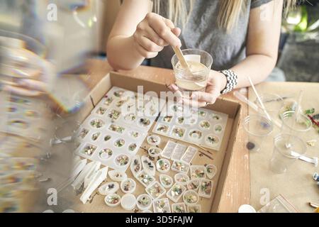 Femme artisan fabriquant des bijoux en résine avec des éléments décoratifs dans un cadre d'atelier Banque D'Images