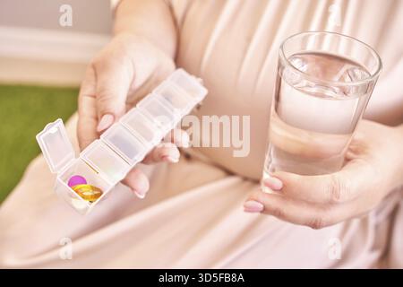 La femme enceinte mange des pilules de grossesse. Suppléments de grippe. Prise de médicaments anti-allergiques. Nourriture médicale oméga 3 de poisson. Corps humain. Buvez de l'eau. Main mère. Malade fema Banque D'Images