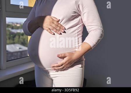 Anticipation tendresse : une mère qui attend sa grossesse par fenêtre ensoleillée Banque D'Images