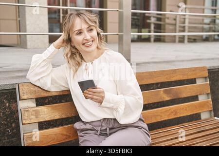 Jolie jeune femme envoyant des SMS par téléphone. Personne féminine heureuse à l'extérieur. Portrait d'affaires d'été. Lady sms amis. Cheveux blonds. De mignons étudiants adultes au remorquage Banque D'Images