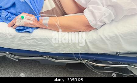 Patient allongé sur le lit d'hôpital avec la ligne IV intraveineuse fixée à la main pendant la procédure de soins médicaux dans un environnement de soins cliniques modernes Banque D'Images