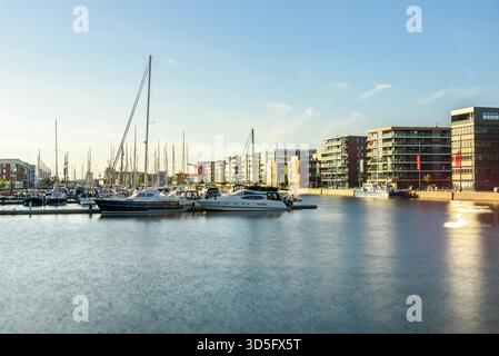 Yachts amarrés aux jetées dans une marina entourée d'immeubles d'appartements modernes au coucher du soleil en été. Exposition prolongée. Banque D'Images
