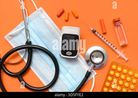 Composition avec oxymètre de pouls, pilules, masque médical et médicaments sur fond orange, gros plan Banque D'Images