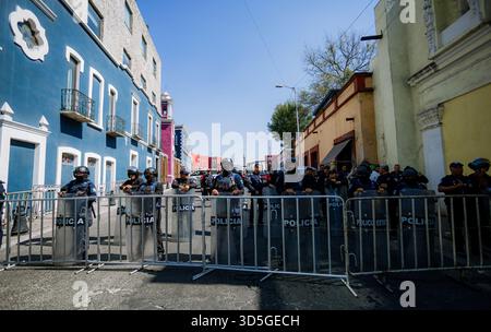 Ligne complète de policiers anti-émeute avec boucliers et casques derrière une barricade métallique, bloquant la circulation dans une rue avec architecte colonial coloré Banque D'Images