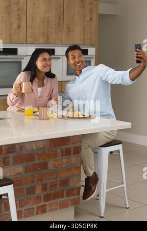 Couple appréciant le petit déjeuner et prenant selfie dans la cuisine moderne, souriant heureux Banque D'Images