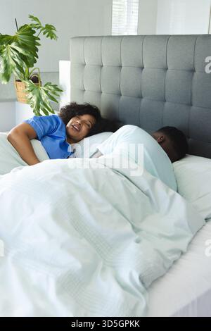Couple afro-américain au lit, femme riant pendant que l'homme dort paisiblement Banque D'Images