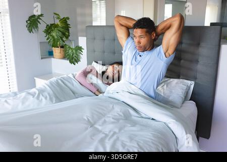 Homme s'étirant dans son lit pendant que la femme dort paisiblement à côté de lui à la maison Banque D'Images