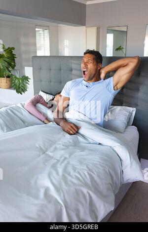 Couple diversifié se réveillant dans une chambre moderne, profitant d'une matinée confortable avec des plantes en pot et un lit gris Banque D'Images