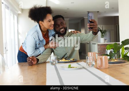 Couple heureux prenant selfie à la maison tout en profitant du petit déjeuner ensemble Banque D'Images