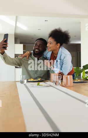 Couple prenant selfie à la table à manger, souriant et profitant du petit déjeuner ensemble Banque D'Images