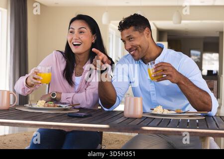 Couple appréciant le petit déjeuner ensemble, souriant et pointant tout en buvant du jus d'orange Banque D'Images