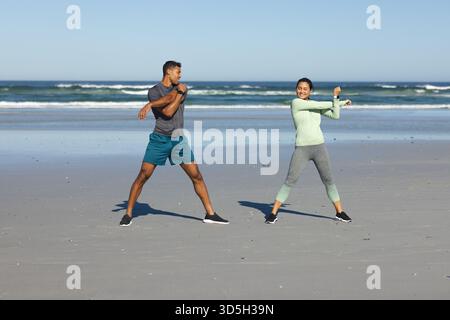 Couple s'exerçant sur la plage, étirant les bras et profitant de l'entraînement matinal ensoleillé Banque D'Images
