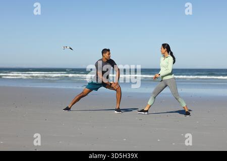 Couple s'exerçant sur la plage, s'étirant et profitant de l'entraînement en plein air ensemble Banque D'Images
