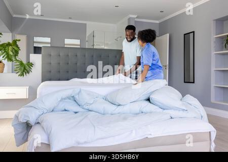 Jeune couple se réveillant dans une chambre moderne sur un grand lit avec oreillers blancs et literie Banque D'Images