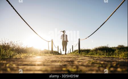Femme courant et s'exerçant sur un chemin en bois avec des cordes encadrant le chemin Banque D'Images