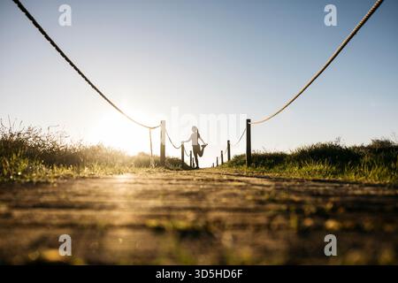Femme effectuant un étirement de quad au coucher du soleil sur un sentier en bois Banque D'Images