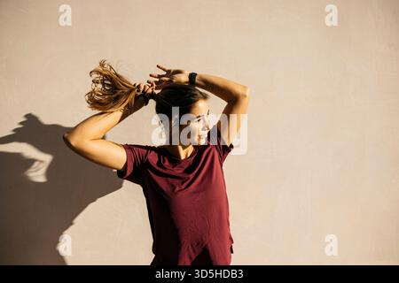 Femme debout à l'extérieur attachant sa queue de cheval se préparant pour une séance d'entraînement Banque D'Images