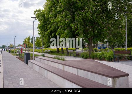 Une large promenade pavée dans une ville, avec des sièges modernes en béton et en bois. Le chemin est bordé de lampadaires et derrière le seati Banque D'Images