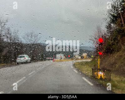 Les gouttes de pluie sur le pare-brise créent un motif abstrait lors de la conduite sur route mouillée avec feu rouge et construction de route en arrière-plan Banque D'Images