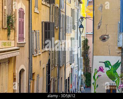 Marseille , France, 10 octobre 2025 : vieux bâtiments colorés bordant une rue étroite avec art de rue dans le quartier panier, marseille Banque D'Images