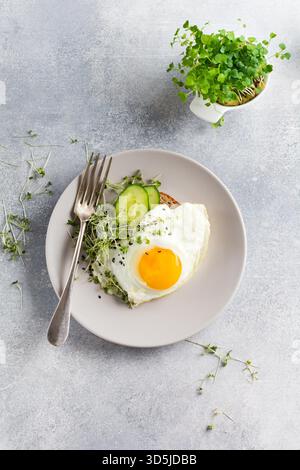 Petit-déjeuner anglais traditionnel avec œufs frits et arugula microgreen dans une plaque en céramique grise sur fond de béton gris ancien. Vue de dessus. Banque D'Images