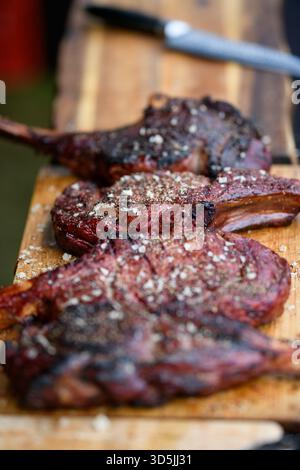 Gros plan de quatre steaks Tomahawk et un couteau sur une planche à découper en bois Banque D'Images