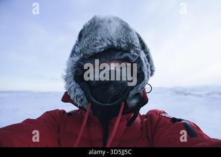 Portrait d'un homme debout dans un paysage enneigé portant une chauve-souris polaire sous une veste gonflante à capuche en fourrure avec seulement ses yeux visibles Banque D'Images
