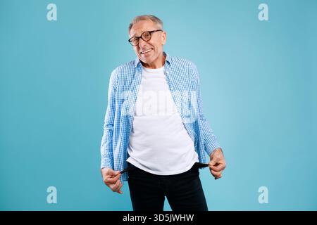 Homme senior montrant des poches vides tout en exprimant son inquiétude au sujet de la situation financière Banque D'Images