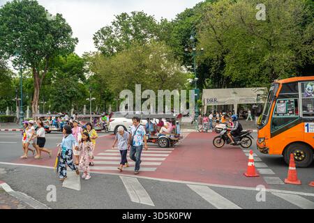 piétons utilisant un passage pour piétons pendant que la circulation, autobus orange, camion de passagers, tuk-tuk, moto passe, Bangkok, thaïlande Banque D'Images