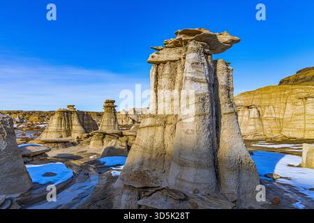 De hauts piliers sculptés de hoodoo contrastent avec des crevasses enneigées et un ciel bleu vif dans les lointaines Bisti Badlands du Nouveau-Mexique. Banque D'Images